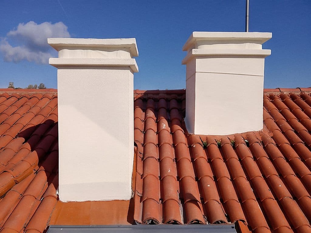 Chimeneas enfoscadas en blanco sobre tejado de teja cerámica curva en Vigo